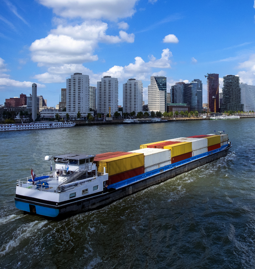 Foto van een containerschip op de Maas met op de achtergrond de skyline van Rotterdam